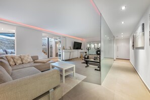 A modern living room with a sofa, a coffee table, and a TV. There is a kitchen area with a fridge, a stove, and a dining table. - Luxury bungalow with heated private pool, sauna & discreet and central location. (Düsseldorf)