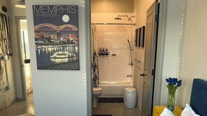 Un dormitorio moderno con una cama grande, vistas a un baño con bañera y ducha, y una obra de arte urbana en la pared.