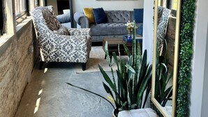 Una sala de estar acogedora con un sofá gris, un sillón estampado y un espejo grande con plantas.