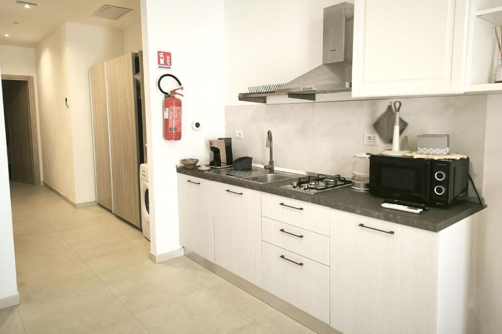 A modern kitchen with a gas stove, microwave, and a sink. There is a fire extinguisher mounted on the wall.