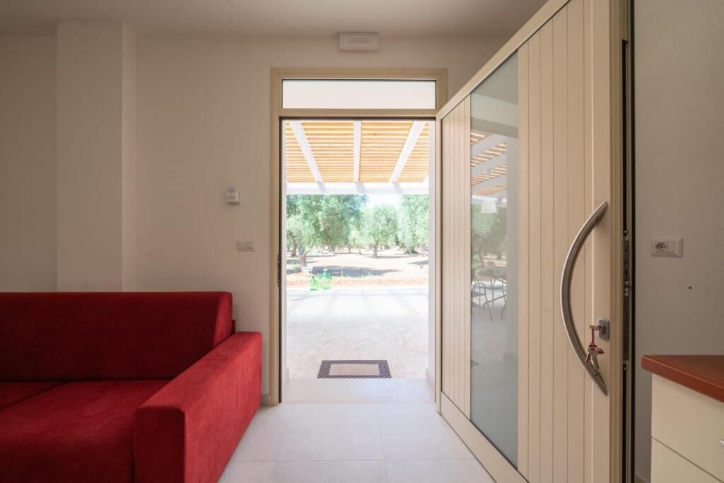 A hallway with a red sofa, a sliding glass door leading outside, and a wooden ceiling structure.