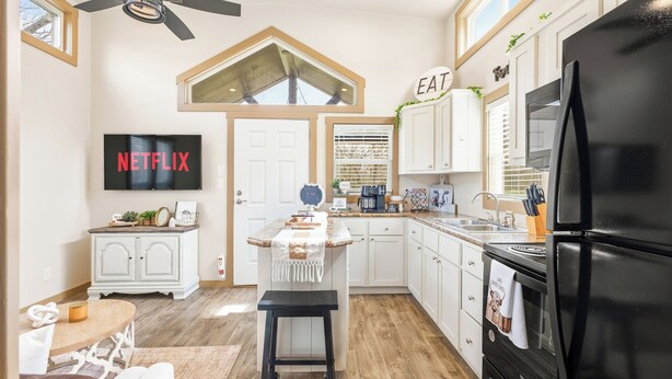 A modern kitchen with white cabinetry, a black refrigerator, and a ceiling fan. - Romantic Tiny Home with Pond, Pier & Firepit (Denison)