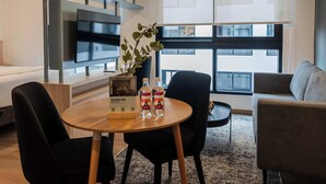 Un salon moderne avec une table ronde en bois, des chaises noires, une plante en pot et un téléviseur à écran plat fixé au mur.