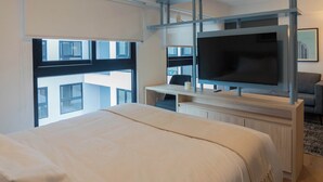 Une chambre d’hôtel moderne dotée d’un grand lit, d’un bureau avec un téléviseur à écran plat et d’un balcon offrant une vue sur la ville.