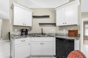 Una cocina con armarios blancos, lavavajillas negro y encimera de granito.