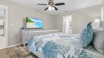 A bedroom with a bed, a ceiling fan, a television, and a dresser.