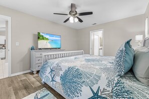 Une chambre à coucher avec un lit, un ventilateur de plafond, une télévision et une commode.