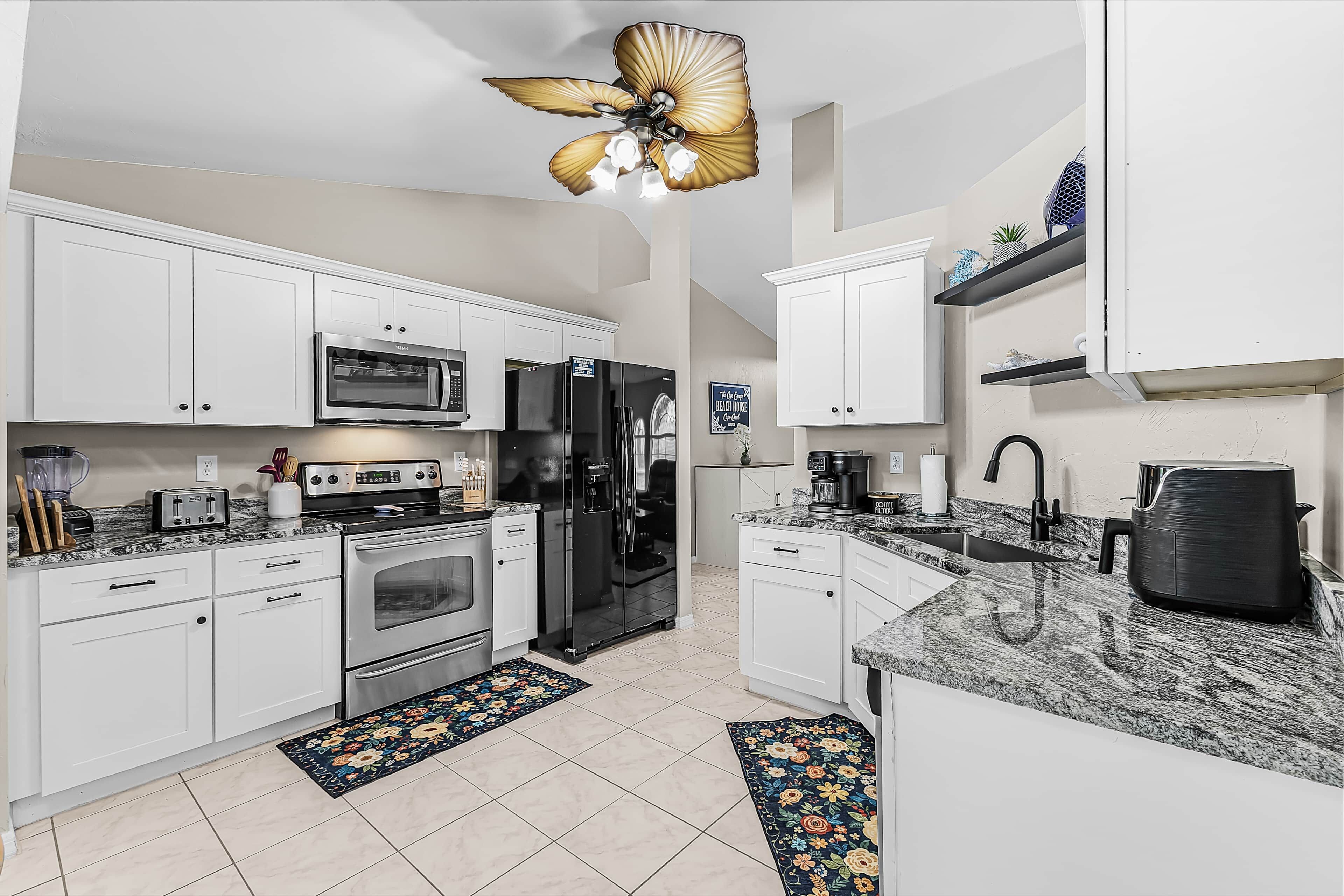 A modern kitchen with white cabinets, stainless steel appliances, a black refrigerator, a microwave, a stove, and a coffee maker.