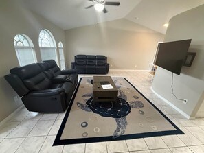 Una sala de estar con un sillón reclinable, un sofá, una mesa de centro y un televisor montado en la pared.