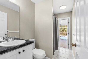 A bathroom with a white sink, toilet, and shower curtain, leading to a balcony with a pool view.