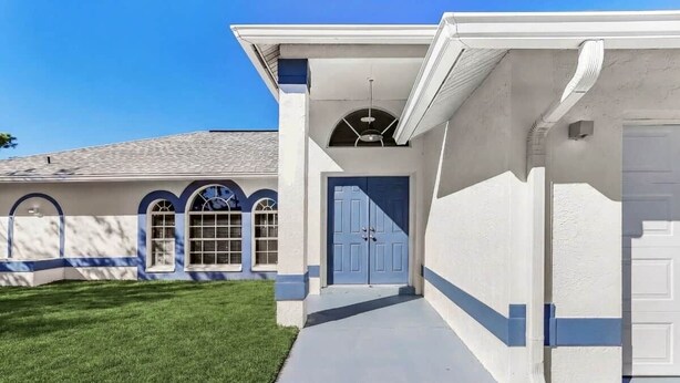 Ein modernes Haus mit einer blauen Tür, einer überdachten Veranda und einem gepflegten Rasen.