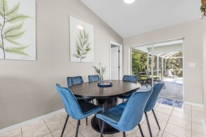 Un coin repas comprenant une table ronde, six chaises bleues à revêtement rembourré et deux reproductions botaniques encadrées accrochées au mur.