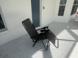 Una silla plegable negra sobre un patio de concreto con un edificio blanco al fondo.