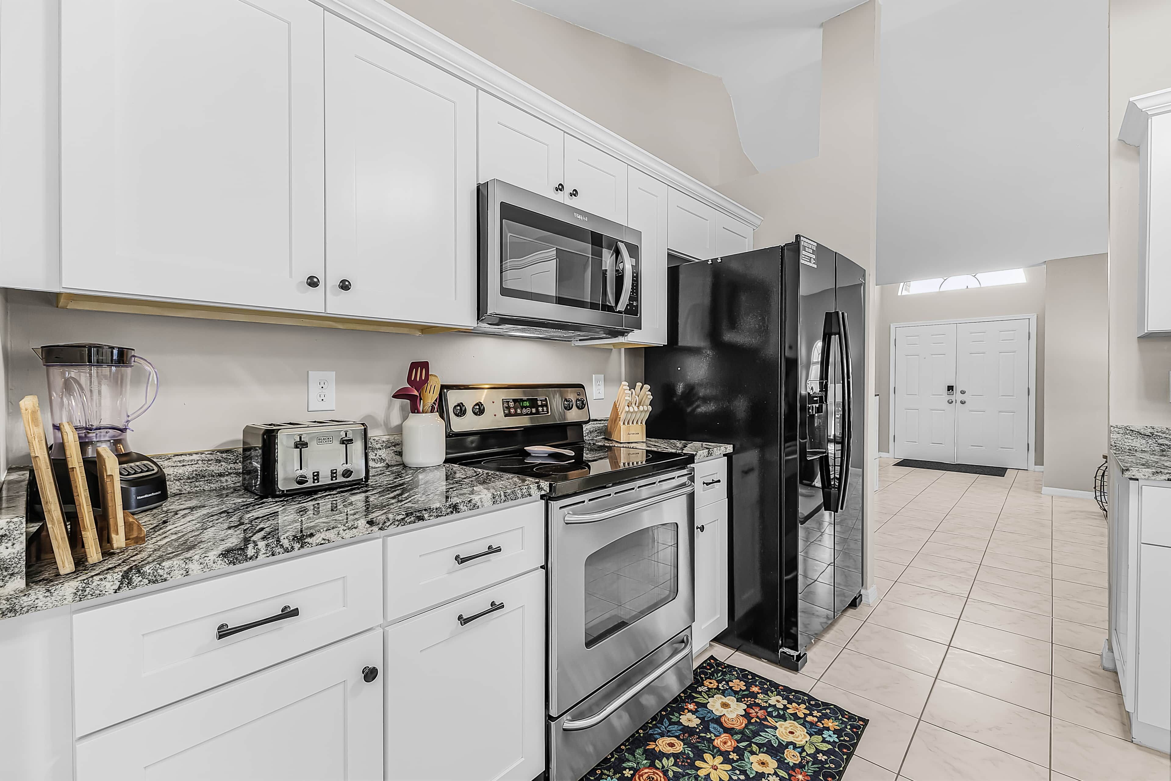 A modern kitchen with white cabinets, a black refrigerator, a microwave, a toaster, and a blender.