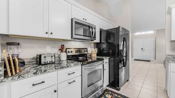 A modern kitchen with white cabinets, a black refrigerator, a microwave, a toaster, and a blender.