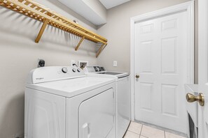 Une buanderie équipée d’un lave-linge et d’un sèche-linge Whirlpool, d’une étagère en bois et d’une porte blanche.