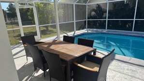 Eine überdachte Terrasse mit Pool, Tisch und Stühlen sowie Blick ins Grüne.