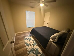 Un dormitorio con cama, ventilador de techo, ventana con persianas y puerta.