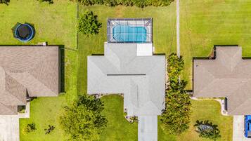 Een woonhuis met een zwembad, een trampoline en een groot gazon.