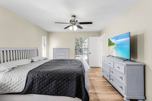 Un dormitorio con cama, ventilador de techo, cómoda, televisor y ventana con persianas.