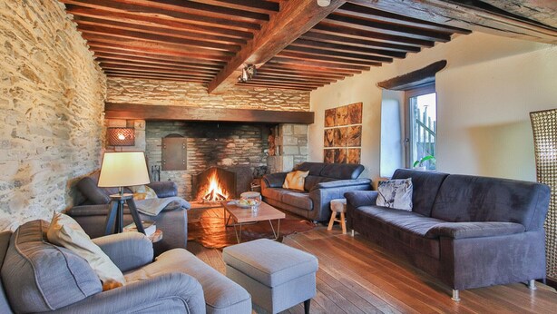 A cozy living room with a stone wall, wooden beams, a fireplace, and comfortable seating. - Nice home in Baraque de Fraiture with sauna (Baraque de Fraiture)