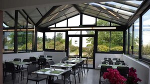 Ein Essbereich im Orangerie-Stil mit Tischen, Stühlen, großen Fenstern und Kübelpflanzen.