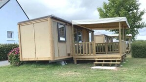 Ein kleiner, hölzerner Caravan mit zwei Räumen, einer Veranda und einem überdachten Bereich.