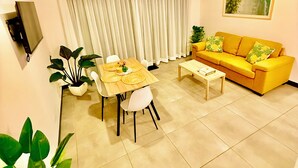 A modern living room with a dining table, yellow sofa, and a TV mounted on the wall.