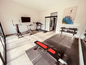 Une salle de sport à domicile équipée de matériel d’exercice, notamment un tapis de course, des vélos d’appartement et un banc de musculation.
