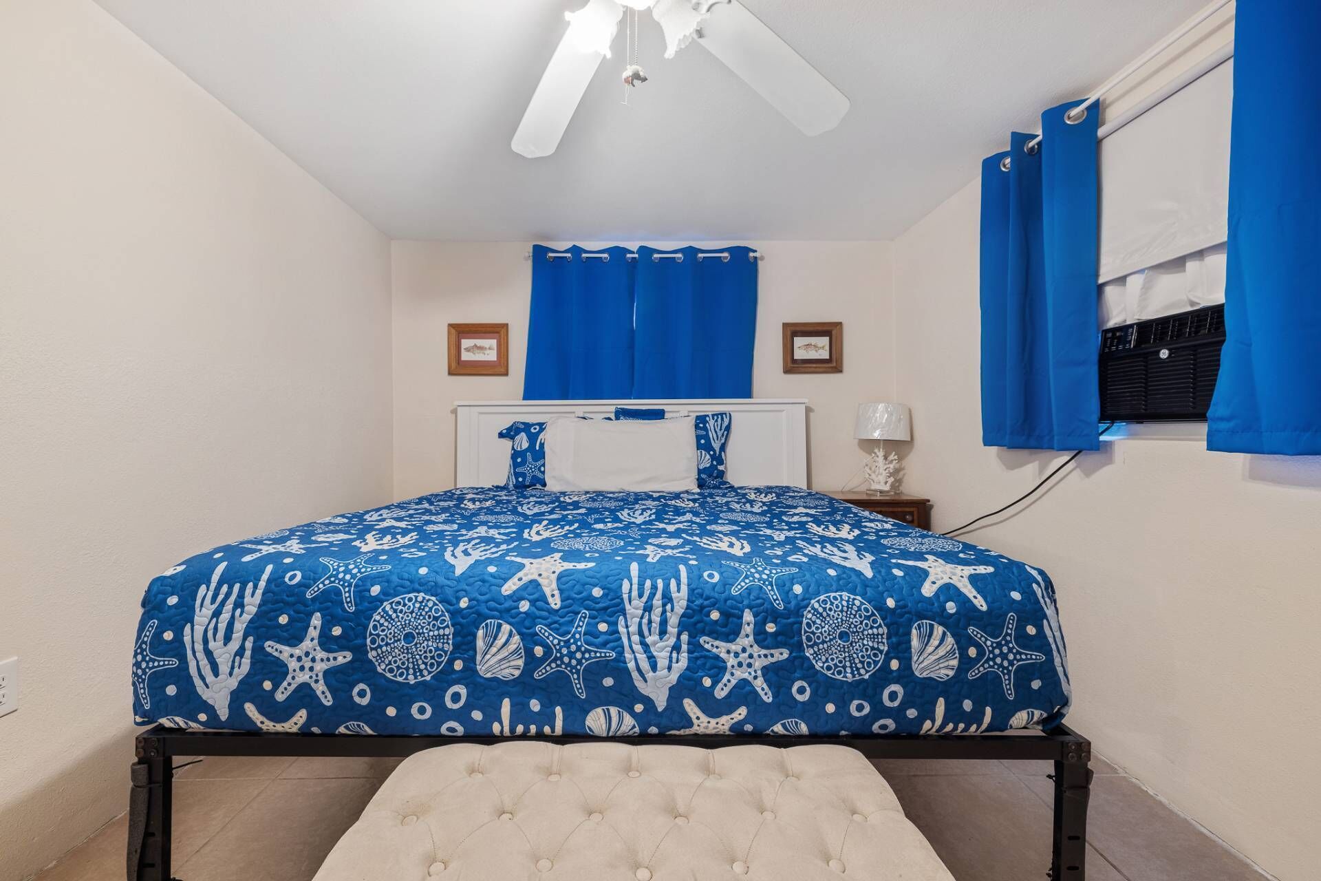 A bedroom with a bed, a ceiling fan, a window with blue curtains, and a wall-mounted heater.