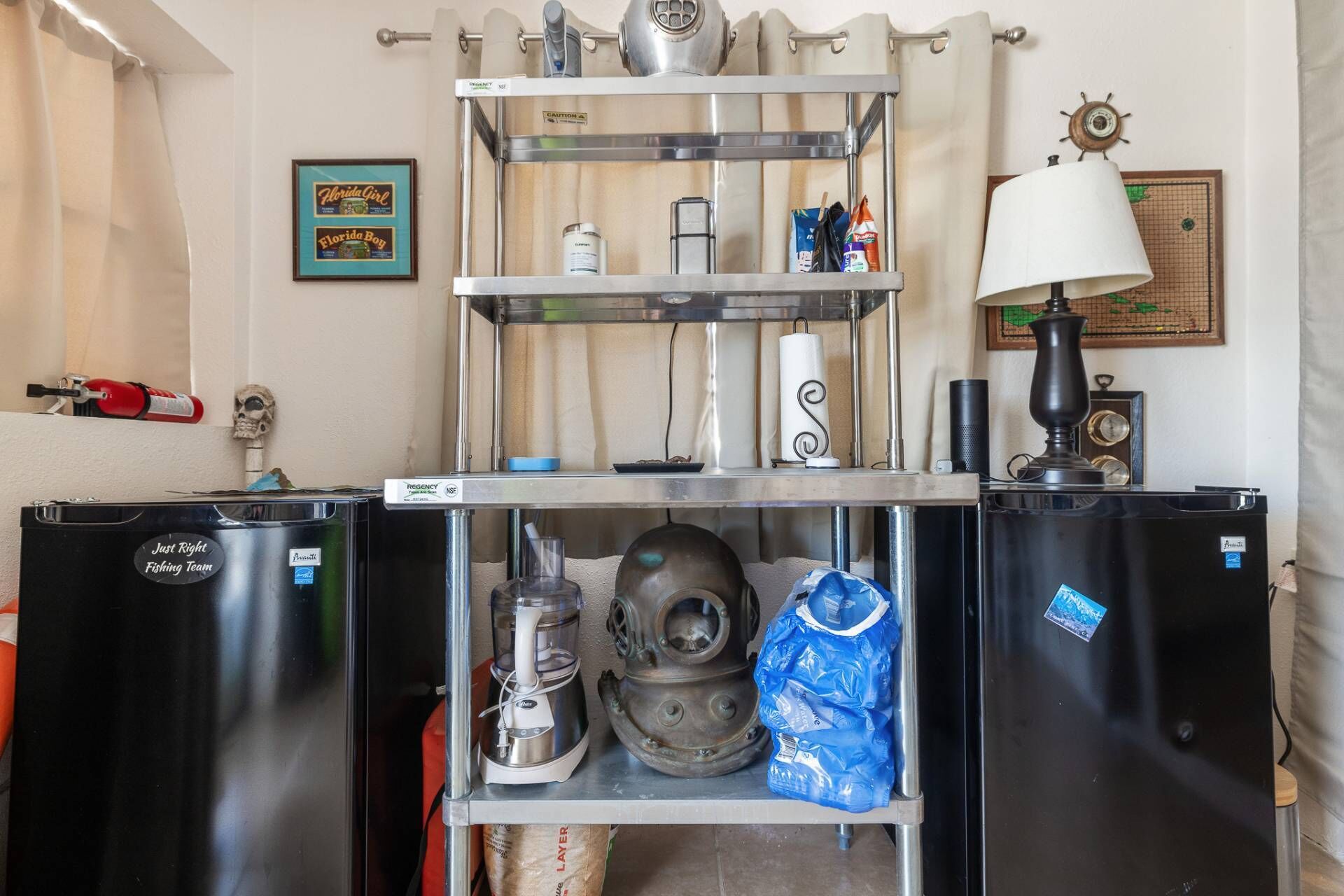 Een keuken met een metalen schapunit, een koelkast en een lamp.