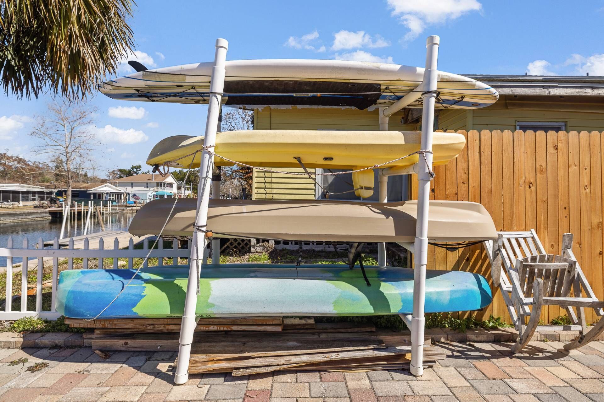 A multi-tiered surfboard rack outdoors with a wooden fence and a house in the background.