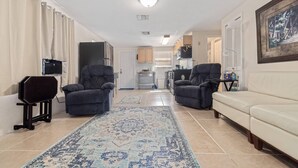 Un espace de vie compact comprenant une cuisine, deux fauteuils, un canapé et un tapis à motifs.