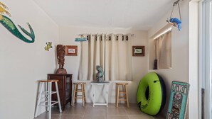 Une pièce avec un sol carrelé, une fenêtre avec des rideaux, un anneau gonflable vert et une petite table avec des tabourets.