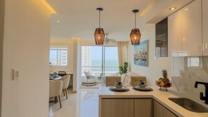 Cozinha moderna com ilha central, iluminação pendente e vista para o mar através de amplas janelas.