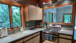 A kitchen with wooden cabinets, a sink, a stove, and a large window. - Tranquil 3-bedroom house with AC in charming Berkshires (Otis)