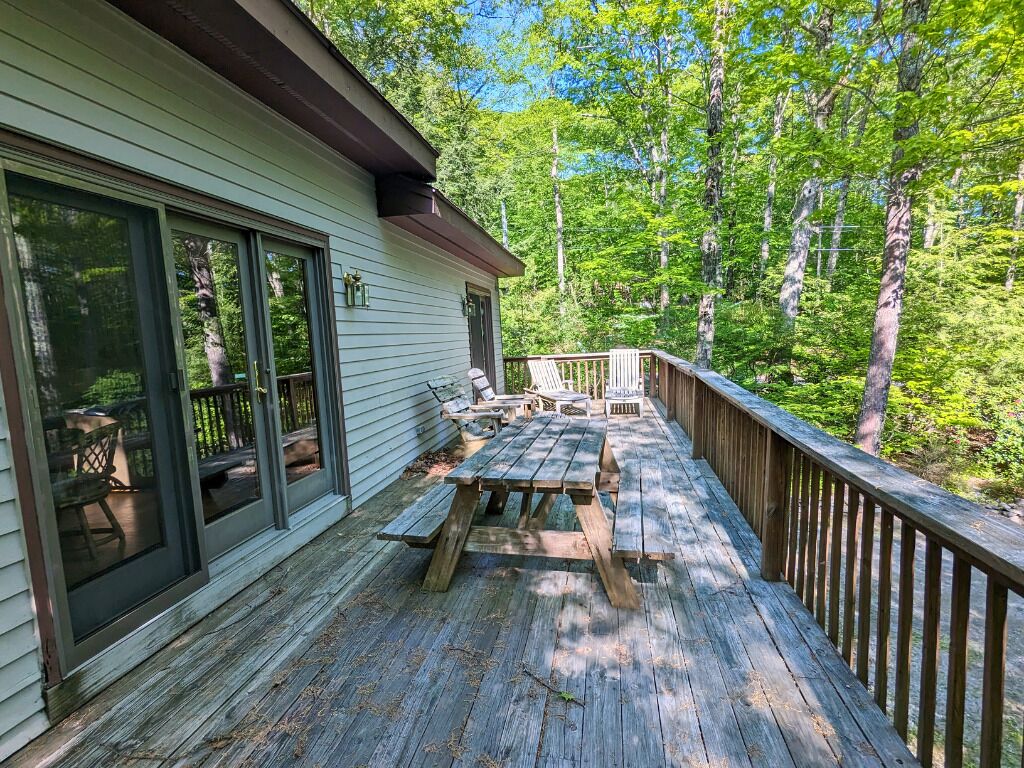 Une terrasse en bois, agrémentée de tables et de chaises pour pique-niquer, entourée d’arbres.