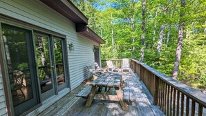 A wooden deck with picnic tables and chairs, surrounded by trees. - Tranquil 3-bedroom house with AC in charming Berkshires (Otis)