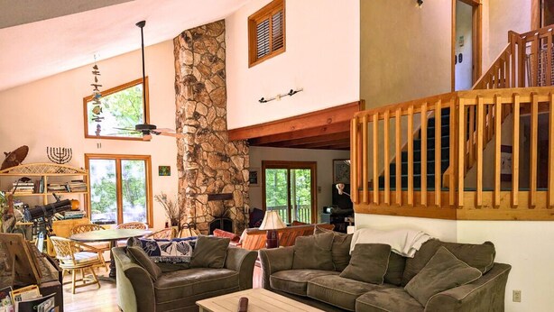 A spacious living area with a stone wall, a wooden staircase, and a large window. - Tranquil 3-bedroom house with AC in charming Berkshires (Otis)