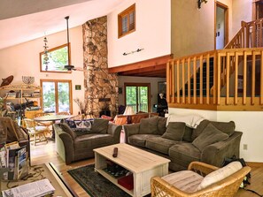 Un amplio espacio habitable con una pared de piedra, una escalera de madera y un gran ventanal.