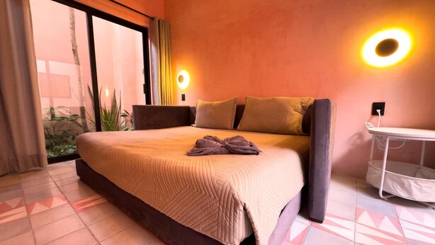A bedroom with a bed, bedside tables, a nightstand, a wall-mounted lamp, and a window with curtains.
