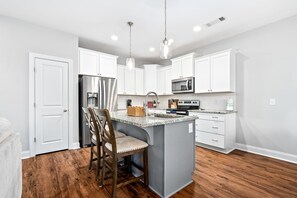 A kitchen with white cabinets, a stainless steel refrigerator, a microwave, and a granite countertop island with bar stools.