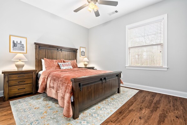 A bedroom with a wooden bed, two bedside tables with lamps, a ceiling fan, and a window with blinds.
