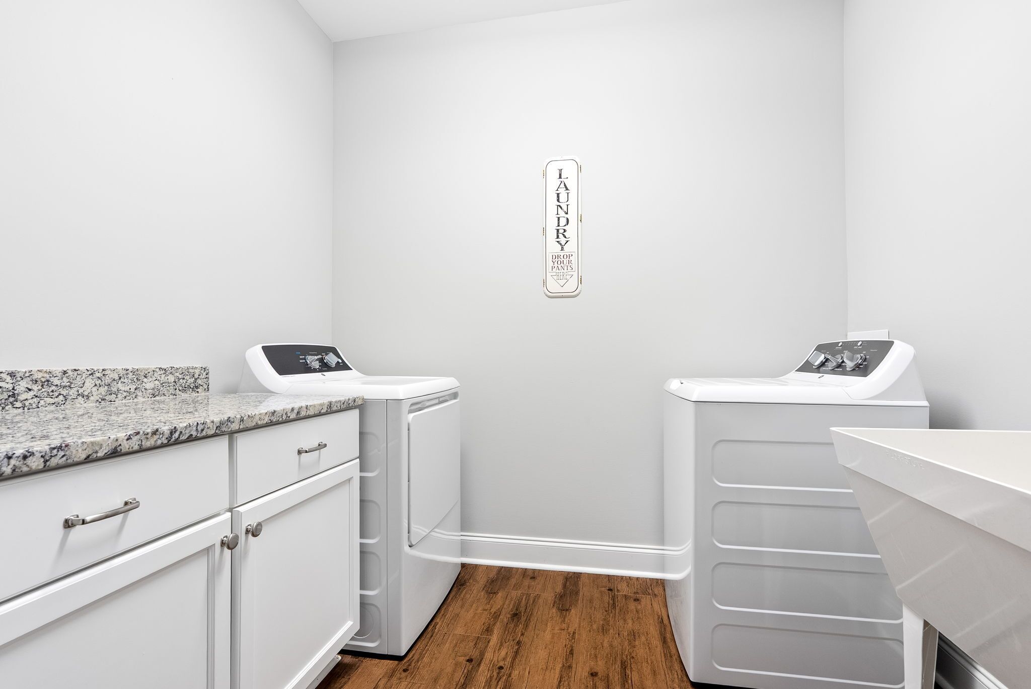 A laundry room with two washing machines, a countertop with a sink, and a wall-mounted laundry instruction sign.