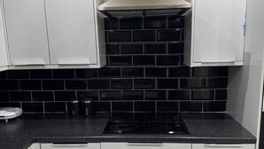 Een keuken met witte kasten, een zwart betegelde achterwand en een roestvrijstalen afzuigkap.