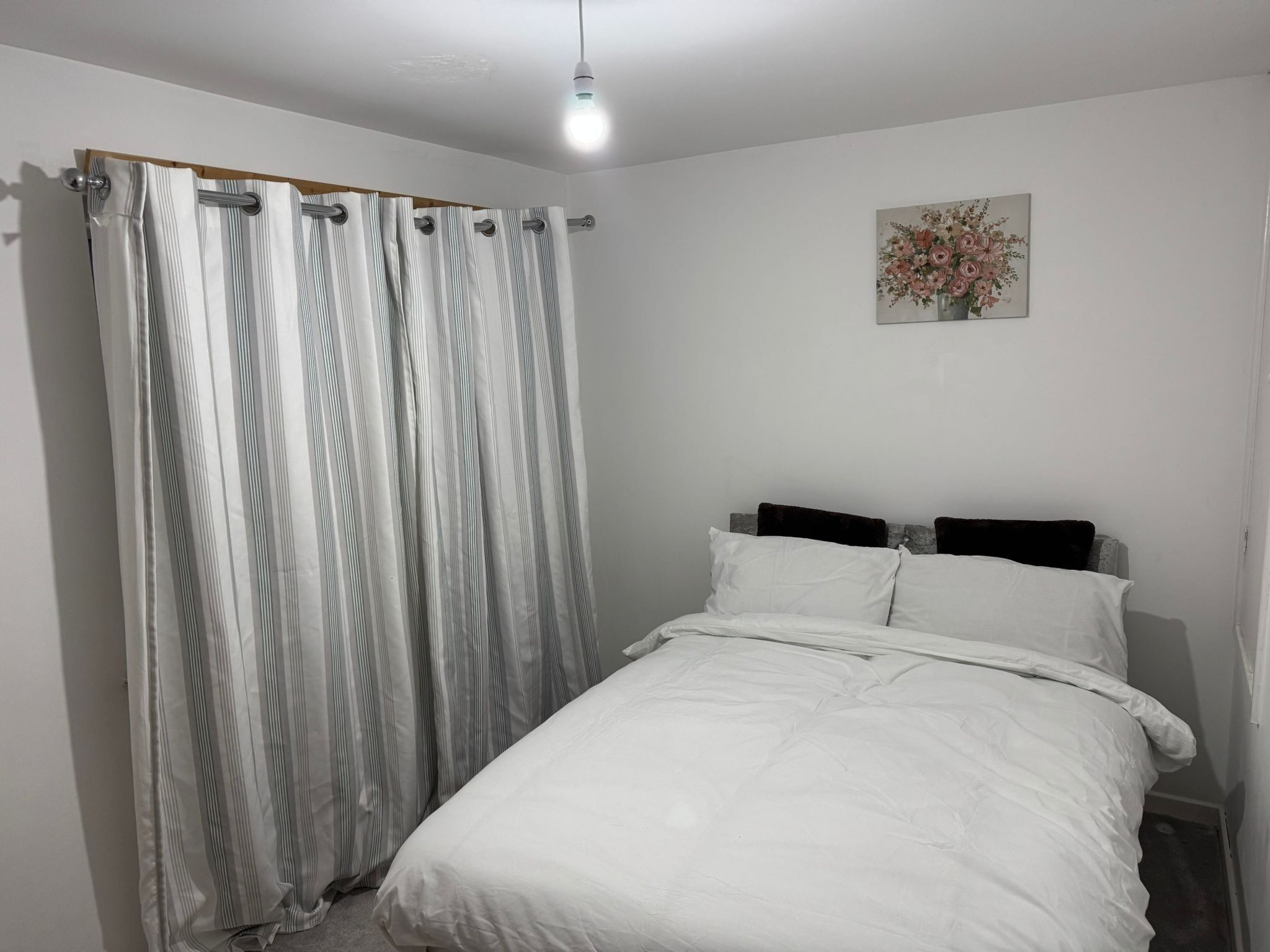 Een slaapkamer met een bed, een gestreept gordijn en een bloemrijk kunstwerk aan de muur.