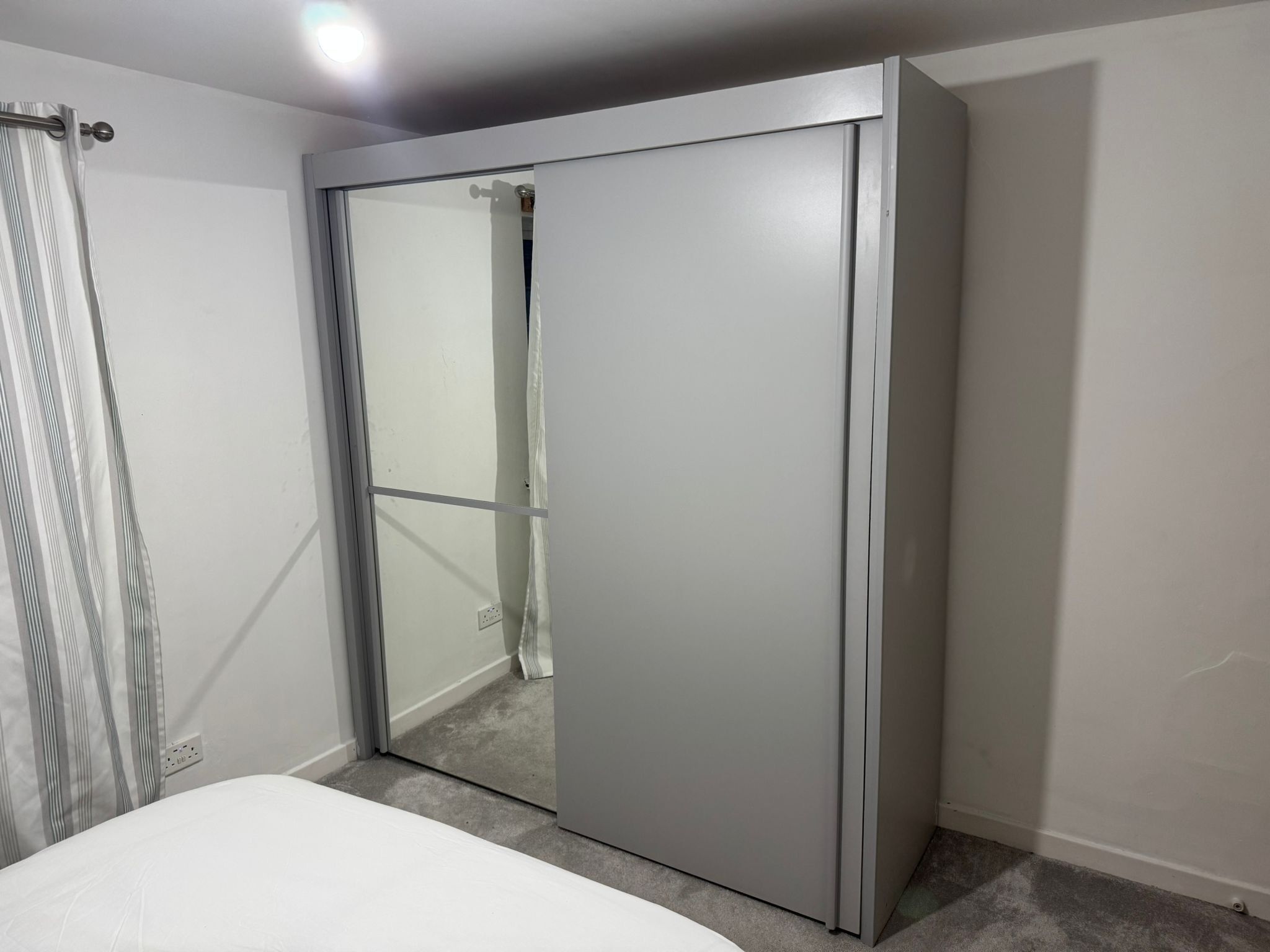 A bedroom with a sliding door closet, a bed, and a curtain.
