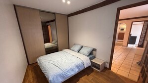 A bedroom with a bed, a nightstand, a mirror, and a wooden floor.