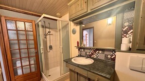 A bathroom with a glass shower enclosure, a sink with a decorative tile backsplash, and wooden cabinets.