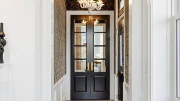 A hallway with a dark wooden door, a chandelier, and patterned wallpaper.